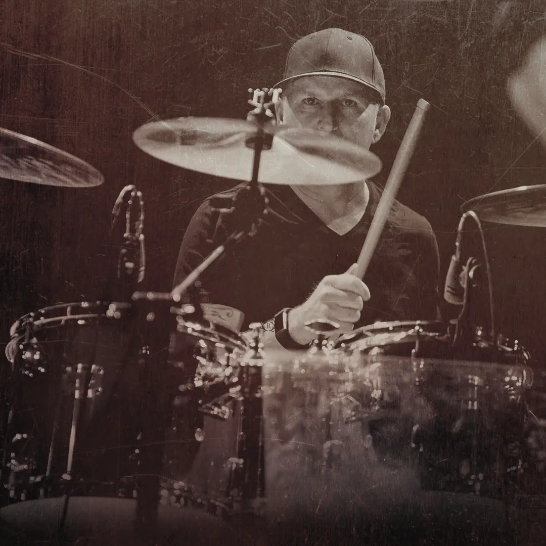 Drummer behind the kit in a ball cap